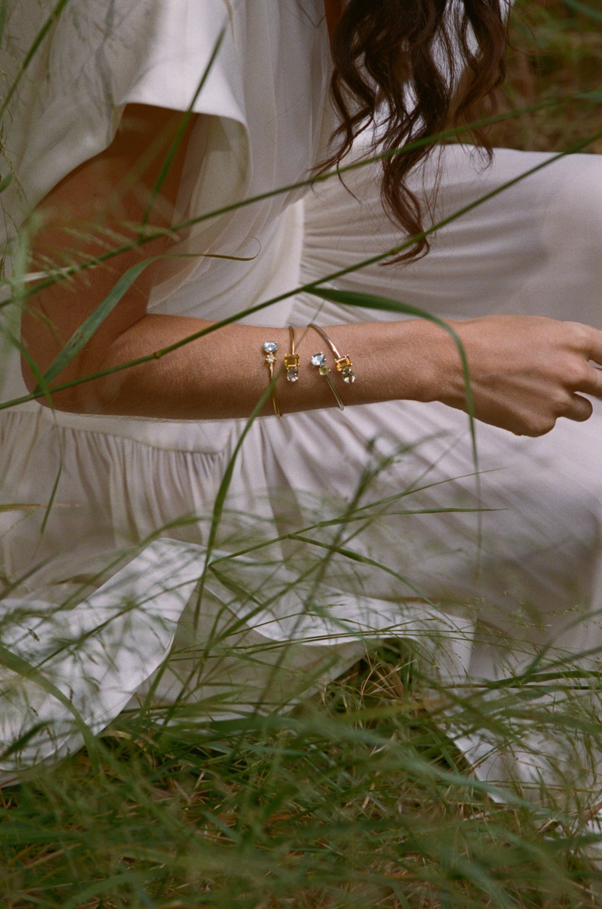 Bracelets collection: gold bangles stacked on a wrist, outdoors in tall grass