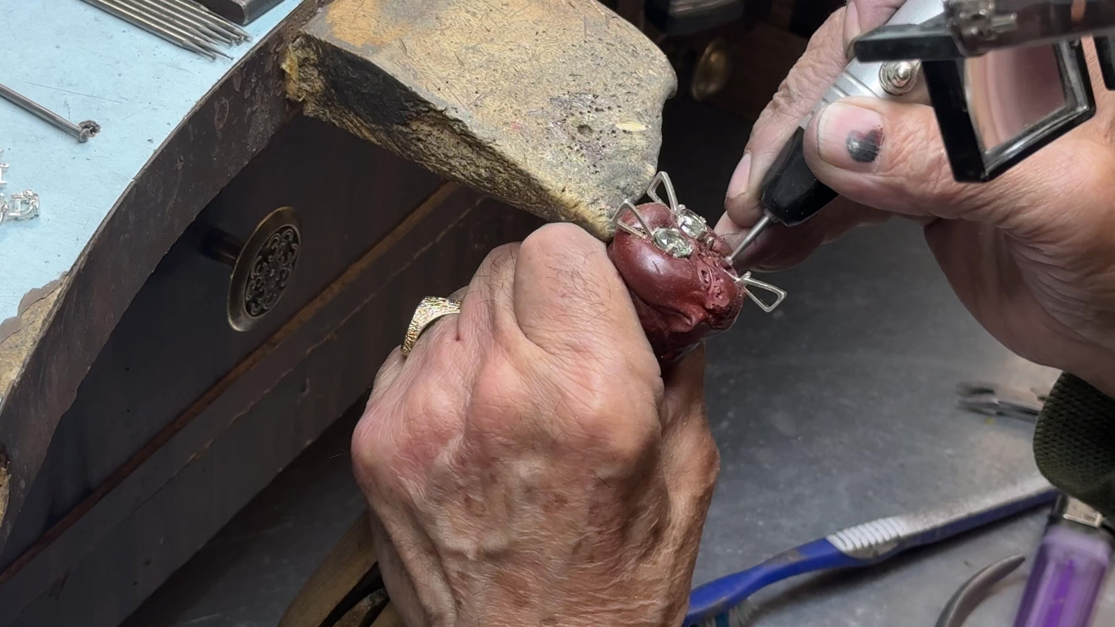 Jeweller's hands setting a stone into a piece at the workbench